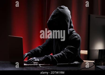 International hacker in black pullover and black mask trying to hack government on a black and red background. Cyber crime . Cyber security. Stock Photo