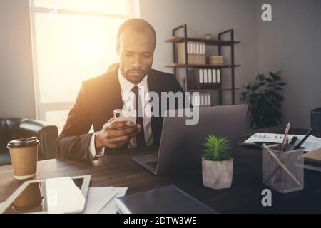 Portrait of focused pensive afro american man broker attorney use smartphone chatting with clients partners wear suit tux tuxedo in workplace Stock Photo