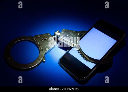 Handcuffs and Mobile Phone on the Blue Paper Background in the Dark closeup Stock Photo