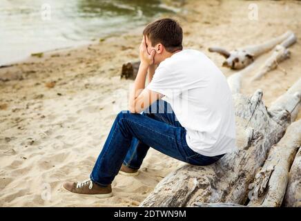 Sad Young Man sit on the Log at the Seaside Stock Photo