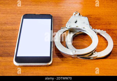 Handcuffs and Mobile Phone on the Wooden Table closeup Stock Photo