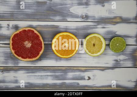 Top down view on four isolated cut fruit halves in a row, red ripe grapefruit, orange, yellow lemon and green lime on white natural wood table with co Stock Photo