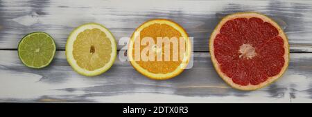 Top down view on four isolated cut fruit halves in a row, red ripe grapefruit, orange, yellow lemon and green lime on white natural wood table with co Stock Photo