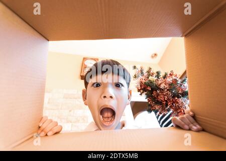 The surprised child unpacking, opening the carton box, and looking inside. The little Asian kid unboxing inside view. Stock Photo