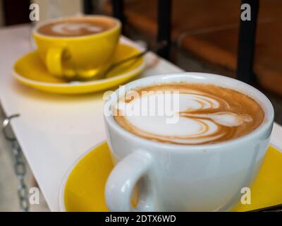 APPETIZING COFFEE DECORATED WITH MILK, IN A YELLOW AND WHITE CUP Stock Photo