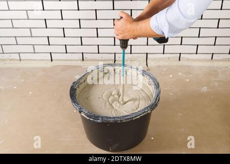 the master mixes the plaster in a bucket. Flat house renovation, master mixed the mortar in a plastic bucket with mixer Stock Photo