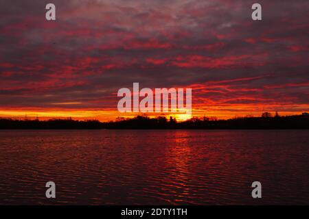 Amazing sunrise or sunset over a lake. Dramatic red sky on the horizon with water on the foreground. Stock Photo