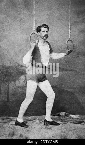 This c. 1872 man was a circus acrobat posing with a pair of rings suspended from the ceiling. In the 1870s, photographers could not take live-action photos at circuses during performances. So any circus performer wanting photographs for himself, or to sell to the public, had to take his costume and equipment to the photographer's studio. This man probably did a number of acrobatic acts, but being an aerialist performing from suspended rings was probably his best and most dangerous act. To see my other circus-related images, Search:  Prestor  vintage  circus Stock Photo