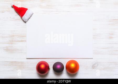Mockup with invitation card on vintage wood background with Santa Claus hat and Christmas balls. Blank greeting card. Minimal Christmas concept. Stock Photo
