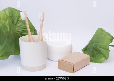 Two eco bamboo zero waste toothbrushes in a glass with organic cosmetics on a white background Stock Photo