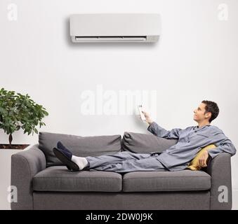 Young man in pajamas with a remote control putting on an air conditioning unit at home Stock Photo
