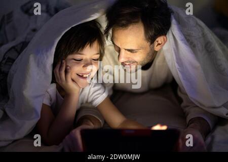 Father and son using digital tablet together at night in bed Stock Photo