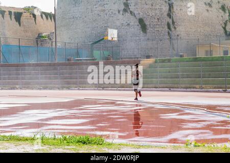 Woman runner jogging on wet red run lane at stadium. Stock Photo