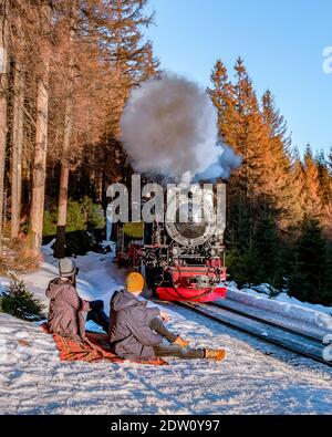 couple men and woman hiking in the Harz national park Germany, Steam train on the way to Brocken through the winter landscape, Famous steam train through the winter mountain. Brocken, Harz Germany Stock Photo
