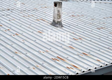 Roof of house made of metal panels. Corrosion exists on roof and old style chimney stack during overcast weather. Stock Photo