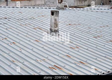 Roof of house made of metal panels. Corrosion exists on roof and old style chimney stack during overcast weather. Stock Photo