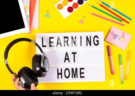 Hand with headphones, lightbox, tablet, school supplies on yellow background. Online learning, education background Stock Photo