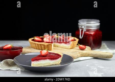 Strawberry summer pie with fresh berries halves and jam in jar on grey stone table on black Stock Photo