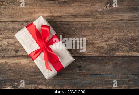 Beige gift box tied with a red ribbon on a wooden background. Top view, with space to copy. Stock Photo