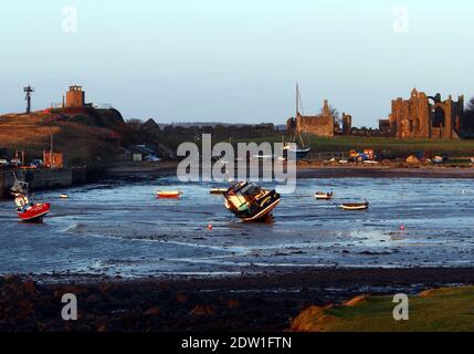 Boats lie on the mud at low tide in Lindisfarne Harbour in the north of Northumberland in England. Stock Photo