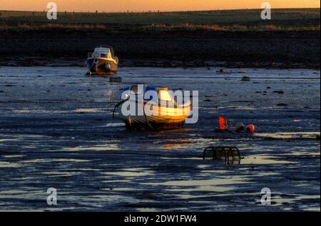 Boats lie on the mud at low tide in Lindisfarne Harbour in the north of Northumberland in England. Stock Photo