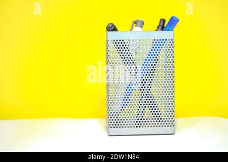 metal gray pencil holder, which is meshed sheet metal. Colorful pencils inside it. Isolated with yellow background. Stock Photo