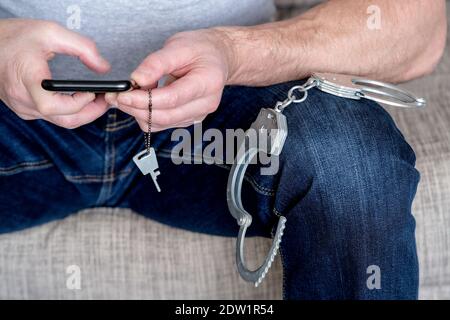 Close-up of handcuffs on the lap of a sitting police officer. In the hands of the phone and the key to the handcuffs. The concept of justice. Preparin Stock Photo