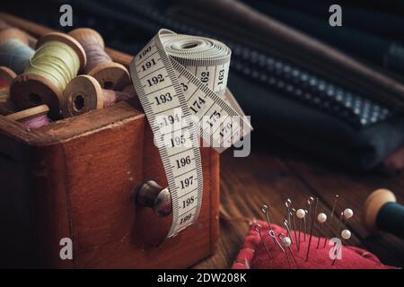 Wooden box of spools of thread, measuring tape, cushion for including pins and stack of fabrics for sewing. Stock Photo