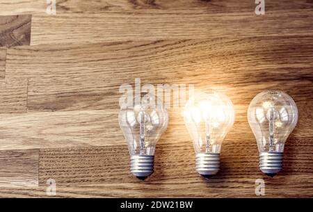Three light bulbs on wooden table, one is lit. Concept for idea, thinking, problem solving Stock Photo