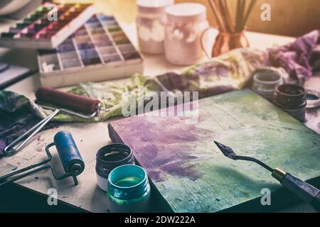 Artistic equipment - canvas and palette knife, paint brushes, multicolored paints in artist studio. Stock Photo