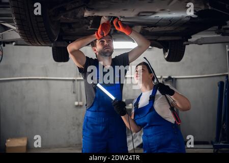 A machinist with a flashlight and a woman in uniform inspect the bottom of the car Stock Photo