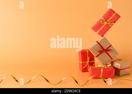 A lot of gift boxes are falling on a yellow background. Gifts wrapped in paper and tied with ribbons, Golden serpentine Stock Photo