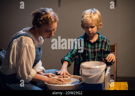 a beautiful woman teacher in her workshop conducts a lesson in clay modeling for a little boy Stock Photo
