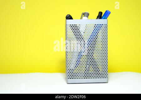 metal gray pencil holder, which is meshed sheet metal. Colorful pencils inside it. Isolated with yellow background. Stock Photo