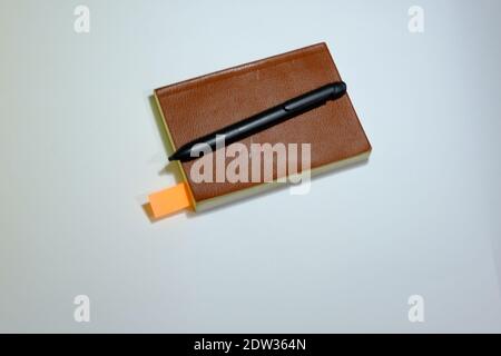 Vintage notebook with brown and leader cover. There is black pen on the notebook and orange bookmarket. Isolated with background. Stock Photo