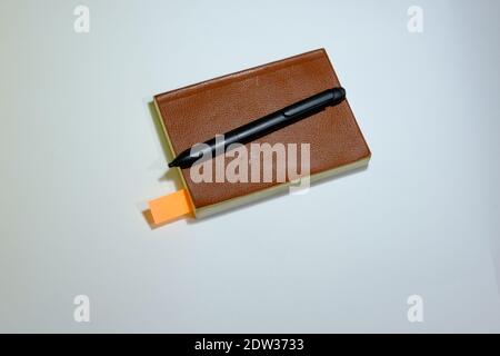 Vintage notebook with brown and leader cover. There is black pen on the notebook and orange bookmarket. Isolated with background. Stock Photo