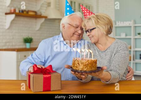 Smiling senior couple sitting with birthday cake and present box and looking at each other Stock Photo