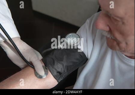 close-up of a doctor using a stethoscope on an elderly person's elbow to measure blood pressure. A gerontologist monitors the health of an elderly pat Stock Photo