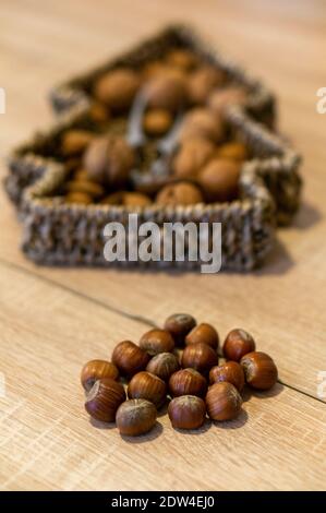 A selective focus shot of a pile of hazelnuts, a Christmas tree-shaped woven basket with mixed nuts in the background Stock Photo