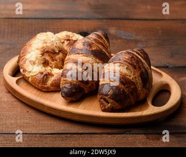 two baked croissants lie on a wooden tray, food on a brown background Stock Photo