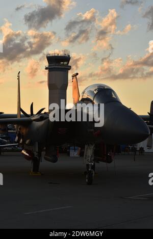 F-15 fighter jet on tarmac in Boeing Plaza at sunset, radio control tower in distance, at EAA AirVenture, Oshkosh, Wisconsin, USA Stock Photo