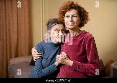 Adult daughter takes care of elderly mother suffering from dementia, old woman ninety years age gray hair and wrinkles on face and sweet kind smile, f Stock Photo