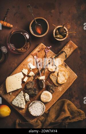 Snacks and appetizers variety for red wine concept. Flat-lay of various cheeses, crackers, smoked meat and glass of red wine on wooden rustic board ov Stock Photo