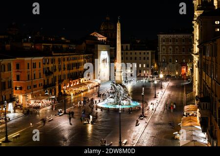 View of the Piazza Navona at night with cafes illuminated and Bernini's Fountain of Four Rivers lit as tourists enjoy the evening. Stock Photo