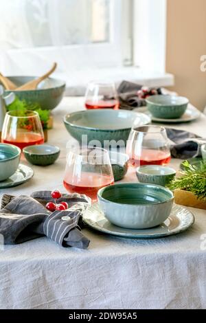 Rustic Christmas table setting with empty craft ceramic tableware, plates and bowls, xmas angel decorations, glasses of red juice, green branches and Stock Photo