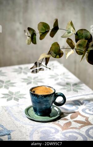 Cup of turkish black frothy coffee on ornate ceramic table with Eucalyptus branches. Sunlight Stock Photo