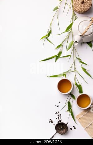 Asian food background set with green tea, cups and teapot with bamboo branches and free space for text on white background. Flat lay Stock Photo
