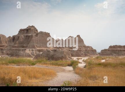 Banded, serrated, mountains of the Badlands Wall in Badlands National Park, South Dakota, with a trail and dried grass in the foreground. Stock Photo