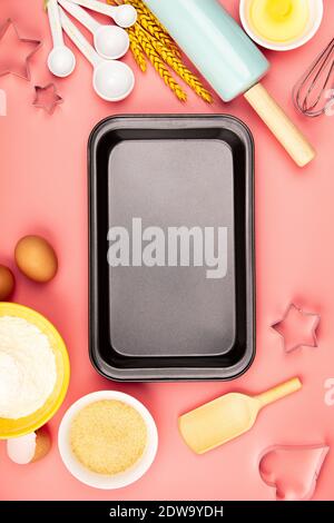 Baking ingredients and empty baking tray on pink background, flat lay. Ingredients, kitchen items for baking. Kitchen utensils, flour, eggs, sugar. Te Stock Photo