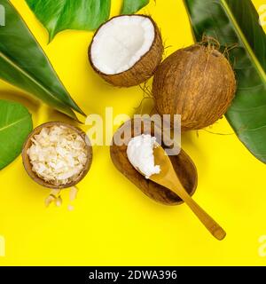 Coconut oil, tropical leaves and fresh coconuts on yellow background, flat lay Stock Photo